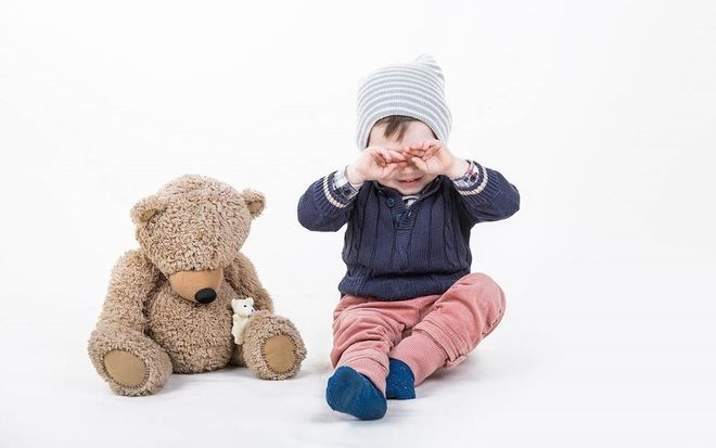 bé trai ngồi dụi mắt bên gấu bông