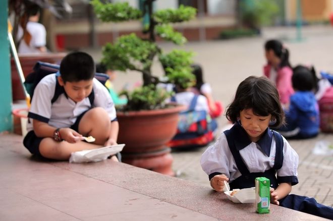 2 bé ngồi ăn ở hành lang trường
