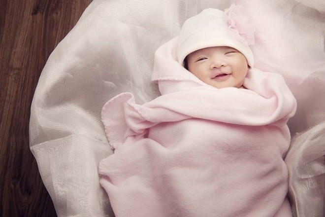 trẻ 2 tháng tuổi nằm cuộn trong chăn mỉm cười