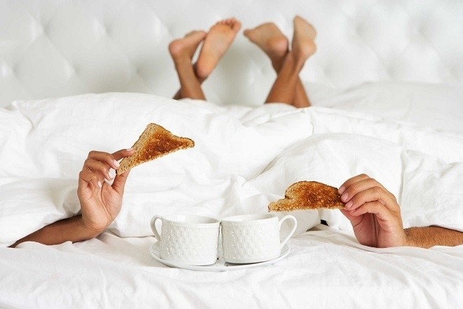 cặp đôi nằm trên giường ăn sáng