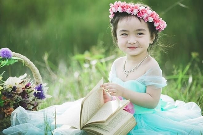 bé gái đầm xanh ngồi ôm sách với thiên nhiên
