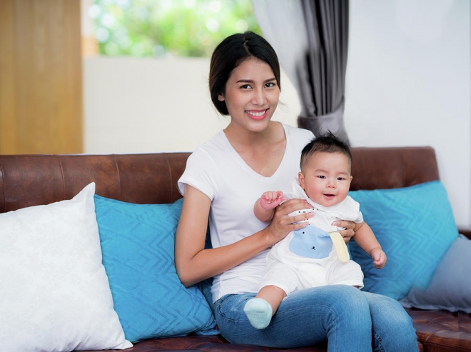 mom and newborn baby sit and play togather on sofa anek suwannaphoom
